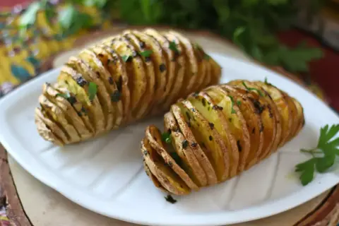 Två gyllene hasselbackspotatis med parmesan och färska örter på en vit tallrik.