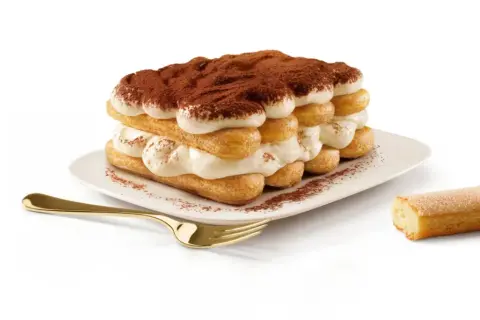Un tiramisu généreux, fait avec 500g de mascarpone, est prêt à être dégusté. Une cuillère dorée et un biscuit à portée de main.