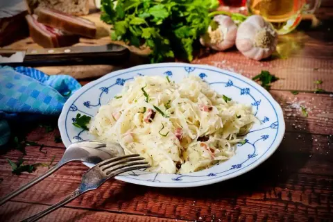 Herzhaftes Krautsalat Rezept mit Speck und frischen Kräutern, serviert auf einem blauen Tellerchen. Dazu Brot, Knoblauch und Petersilie.
