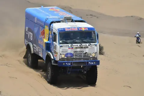 Camion Kamaz aux couleurs Red Bull, prêt à affronter le désert. La puissance camion Dakar se révèle dans ce paysage sablonneux.