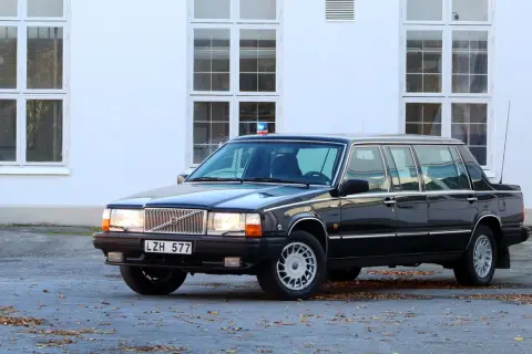 Svart, förlängd 760 Volvo med blåljus på taket, parkerad framför en vit byggnad med stora fönster.