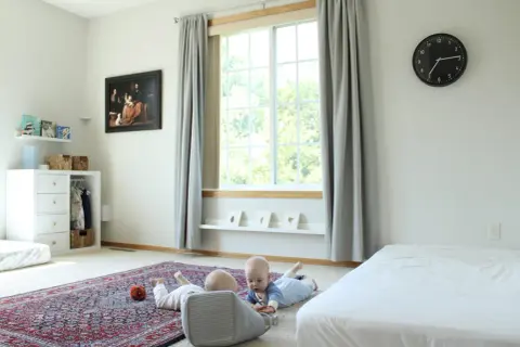 Two babies explore a room with a Montessori inspired feel, featuring a rug, toy basket, and artwork.