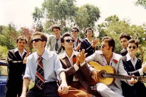Grupo de hombres con trajes, uno toca la guitarra, listos para una rumba catalana bajo el sol.