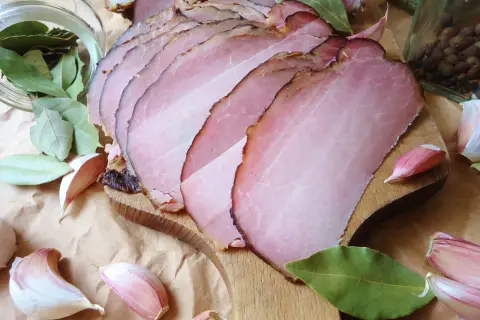 Pokrojony w plastry schab po wędzeniu, otoczony liśćmi laurowymi, czosnkiem i pieprzem.