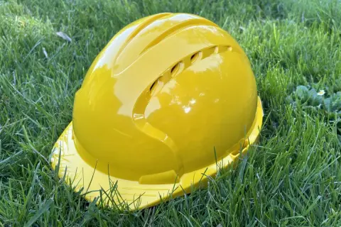 Żółty kask ochronny leży na trawie. Pamiętaj o sprawdzeniu **daty ważności kasku ochronnego** przed użyciem.