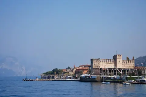 Rocchetta di Moniga del Garda, un gioiello da vedere sul lago. Passeggiata sul lungolago con barche e montagne sullo sfondo.