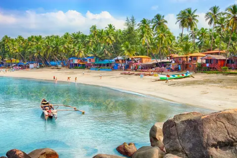 Goa kiedy jechać? Słoneczna plaża z palmami, kolorowe chatki i łodzie. Idealne miejsce na wakacje.