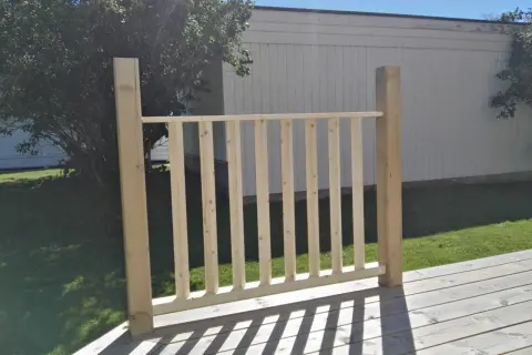 Nybyggt räcke med plank stående ribbor på en altan. Solen kastar skuggor över träet.