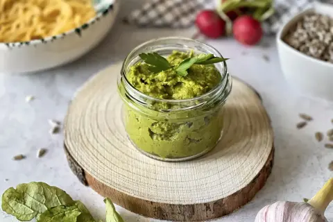 Domowe, tradycyjne pesto przepis. Zielona pasta w słoiczku, obok czosnek, rzodkiewki i nasiona słonecznika.