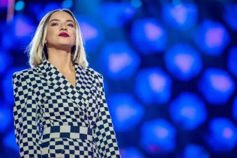Młoda, amerykańska piosenkarka country w stylowej, szachownicowej marynarce na tle niebieskich świateł.