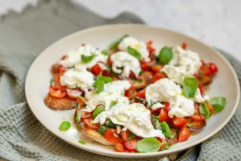 Bruschetta med burrata, färska tomater och basilika på en tallrik.