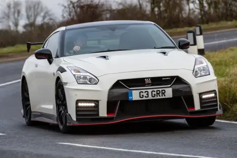 Biały Nissan GT-R Nismo z czerwonymi akcentami pędzi po mokrej drodze, kierowca w środku.