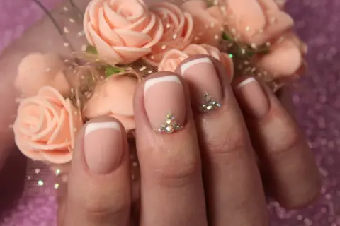 Elegancki french manicure z kryształkami, idealny na francuski swiateczny bal. Delikatne róże w tle dodają uroku.