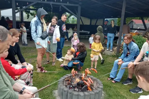 Rodzina piecze kiełbaski nad ogniskiem, czuć puls miasta w tej sielskiej atmosferze.