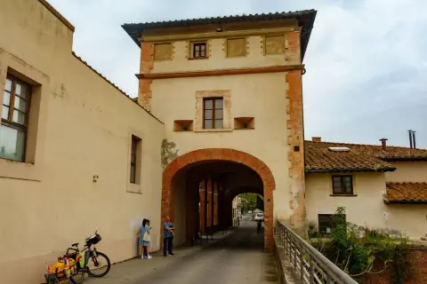Pieve a Nievole: un arco in mattoni rossi conduce a una strada con case antiche. Una coppia e una bici con carretto attendono.