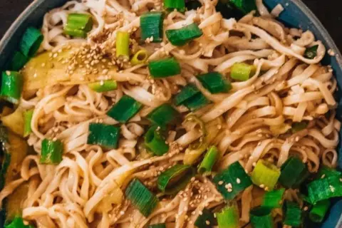 Schüssel mit Udon-Nudeln, garniert mit Frühlingszwiebeln und Sesam. Ein einfaches Udon-Nudel-Rezept, das schnell zubereitet ist.
