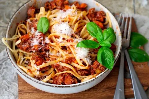 Eine Schüssel mit Linguine und einer herzhaften, **schnellen Bolognese**, garniert mit frischem Basilikum und Parmesan.