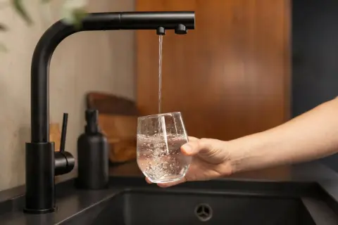 Un robinet noir verse de l'eau dans un verre, promettant une eau moins calcaire pour une boisson pure et rafraîchissante.