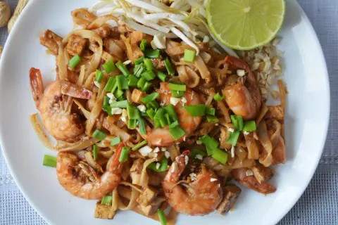 Pyszny pad thai kung z krewetkami, tofu i szczypiorkiem, podany z kiełkami fasoli mung i ćwiartką limonki.