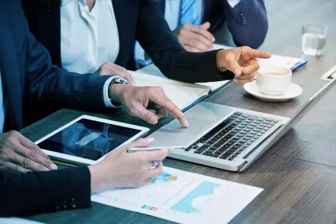 Persone in abiti eleganti collaborano a un tavolo, analizzando dati su tablet e laptop. Sono le risorse umane che lavorano insieme per il successo.