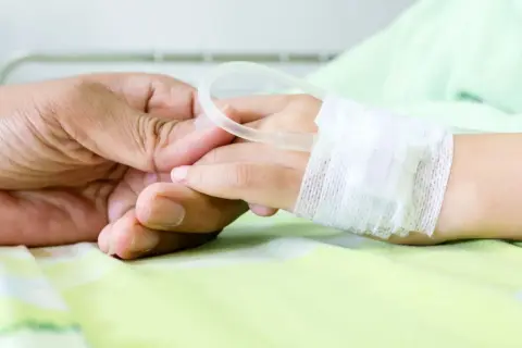 Dłoń rodzica trzyma dłoń dziecka w szpitalu, gdzie wystawiane jest zwolnienie na dziecko w szpitalu.