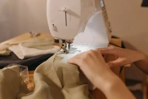 Ręce prowadzą materiał pod maszynę do szycia, by nauczyć się, jak zwęzić sukienkę w ramionach.