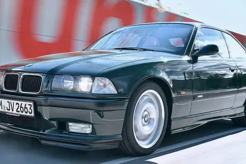 Klasyczne BMW E36 w kolorze ciemnej zieleni pędzi po drodze.