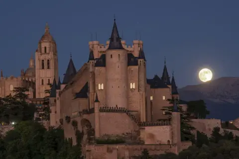 El majestuoso castillo de Segovia se alza bajo una luna llena, con su imponente arquitectura y torres que parecen vigilar la noche.