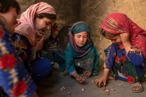 Vier Mädchen spielen mit Steinen. Ihre Kleidung und Kopftücher spiegeln die afghanische Kultur wider.