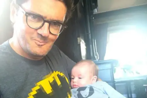 Kuba Wojewódzki z dzieckiem na rękach, w koszulce z Batmanem. Czy Kuba Wojewódzki ma dzieci? Tak, to dowód!