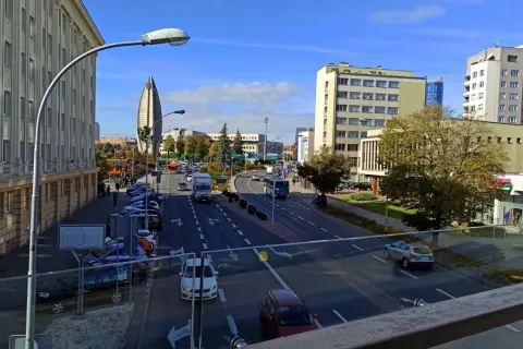 Widok na ruchliwą ulicę w Rzeszowie, z charakterystycznym budynkiem przypominającym żagiel w tle. W oddali widać **ogrody bernardyńskie rzeszów**.