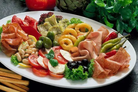 Eine reichhaltige Antipasti-Platte mit Wurst, Käse, Gemüse, Oliven und Brotstangen.