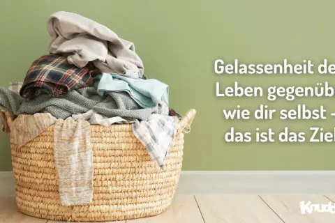 Ein Wäschekorb voller Kleidung vor einer grünen Wand. Der Spruch "Gelassenheit dem Leben gegenüber wie dir selbst – das ist das Ziel" lädt dazu ein, das eigene Bewusstsein zu erweitern.