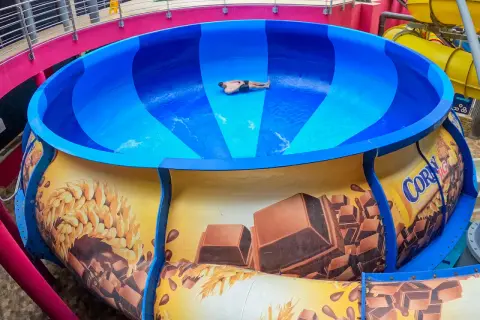 Mann rutscht in einer riesigen blauen Schüssel einer Wasserrutsche, die mit Schokolade und Getreide dekoriert ist. Ein Spaß im Prag!