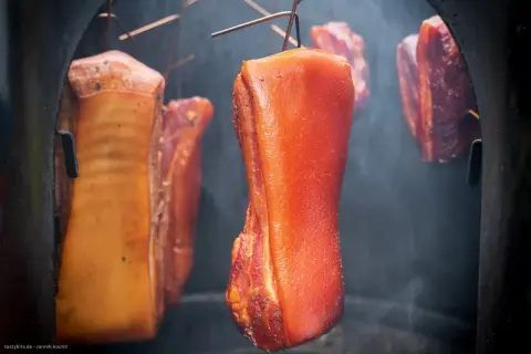 Fleischstücke hängen im Rauch, bereit für das **bacon selber machen**. Der Prozess des Räucherns verleiht dem Speck seine charakteristische Farbe und Aroma.