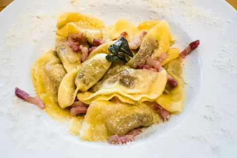 Deliziosi ravioli bresciani conditi con pancetta croccante e una foglia di salvia, spolverati di parmigiano.
