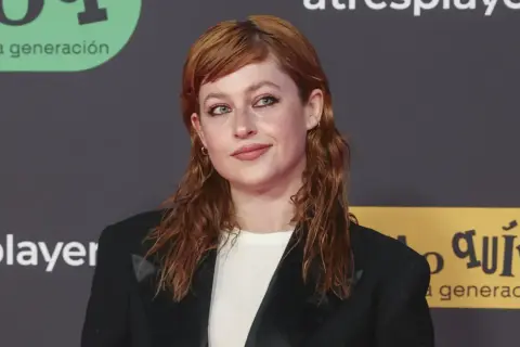 Chloe Wallace, con su cabello pelirrojo y mirada cautivadora, posa con un blazer negro.