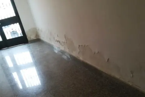 Pared con pintura descascarada y manchas de humedad por capilaridad cerca de la puerta. Es necesario reparar la pared.