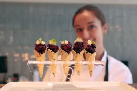 Cinco conos de gofre con tartar de remolacha y cubitos de manzana, presentados en un soporte con el logo Robuchon.