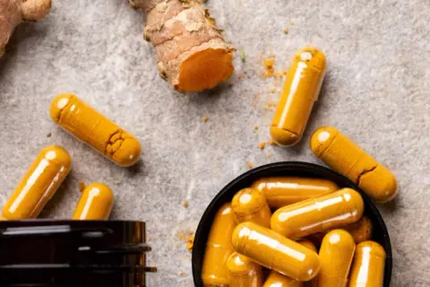 Curcuma-Kapseln und frische Wurzeln. Entdecke, was bewirkt Curcuma für dein Wohlbefinden.
