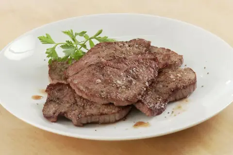 Saftiges Schnitzel Natur, gewürzt mit Pfeffer und Salz, auf einem weißen Teller mit Petersilie garniert.