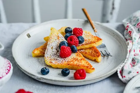 Goldbraune French Toast-Scheiben, bestäubt mit Puderzucker und garniert mit frischen Beeren. Ein perfektes Frühstück, das Lust auf mehr macht.