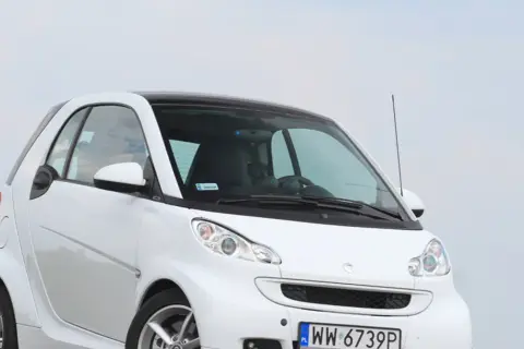 Biały smart fortwo 451 z czarnym dachem, zaparkowany na tle nieba.