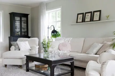 Gemütliches Wohnzimmer mit einem Sofa und Sessel in off white farbe, einem schwarzen Schrank und einem Couchtisch.