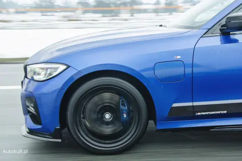 Niebieskie BMW 330e z napisem M Performance na progu, w ruchu drogowym.