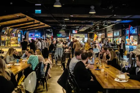 Tętniący życiem food hall Metropolia, gdzie ludzie jedzą i piją przy długich stołach, a w tle widać bary i stoiska z jedzeniem.