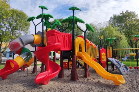Kolorowy plac zabaw z zjeżdżalniami, drabinkami i huśtawkami na piasku.
