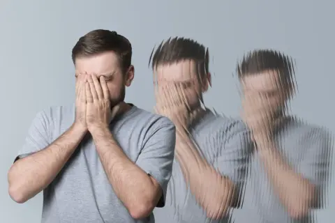 Mężczyzna z rękami na twarzy, doświadczający wizualnych zaburzeń, jak przy delirium tremens.