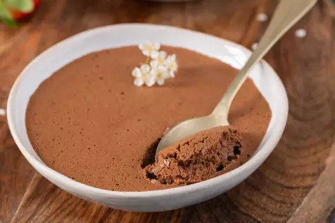Une cuillère prend une bouchée d'une délicieuse mousse au chocolat, garnie de petites fleurs blanches.
