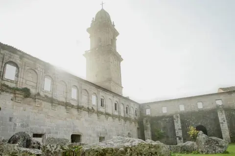 El imponente **monasterio de Oia** se alza bajo un cielo brumoso, con su torre campanario y sus muros de piedra evocando historias de siglos pasados.
